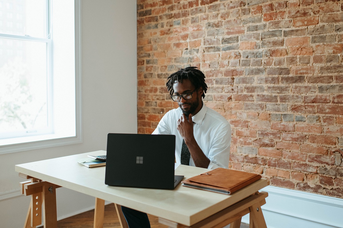 Imagem de um homem negro trabalhando num computador que está sobre uma mesa de madeira